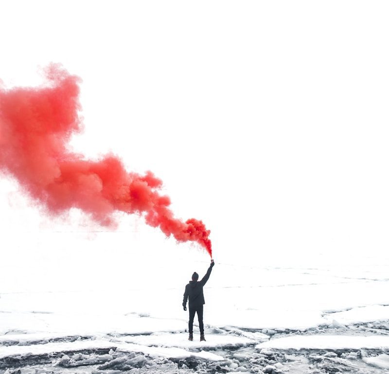 selective color photography of person holding orange gas smoke standing on snow