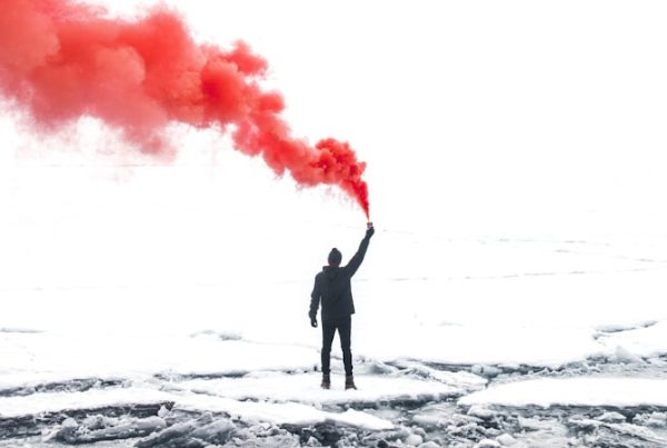 selective color photography of person holding orange gas smoke standing on snow