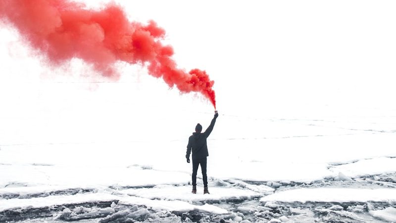 selective color photography of person holding orange gas smoke standing on snow